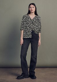 Svart och krämfärgad mönstrad blus med V-ringning och uppvikt ärm, parat med högmidjade mörka jeans och kraftiga svarta skor.