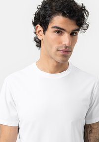 T-shirt en coton blanc avec un col rond et des manches courtes. Le tissu a une texture lisse et est ajusté. Aucuns motifs ou graphiques visibles.