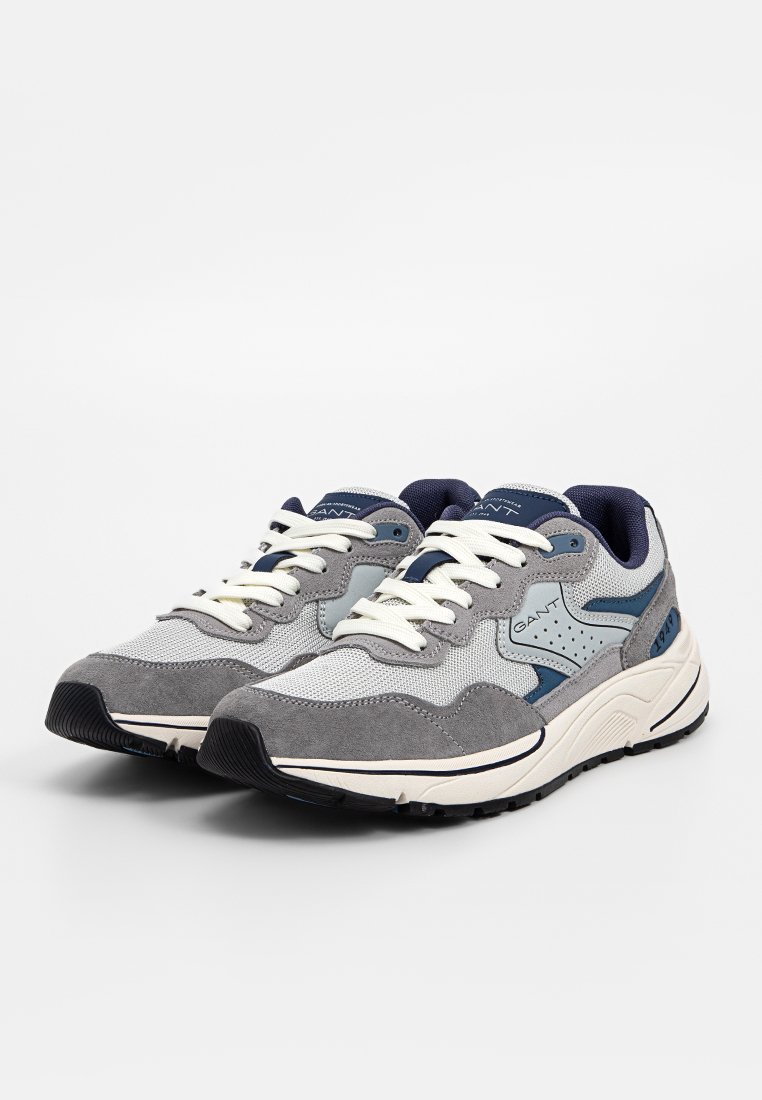 Graue und marineblaue Sneakers aus Mesh- und Wildledermaterial, mit weißen Schnürsenkeln, texturierten Akzenten und einer Gummisohle.