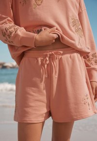 Felpa di cotone rosa chiaro con ricami floreali e pantaloncini abbinati con vita elasticizzata e coulisse decorativa.