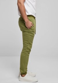 Grüne Jogginghosen aus weichem Material mit zulaufenden Beinen, Seitentaschen und elastischem Bund. Kombiniert mit weißen Sneakern.