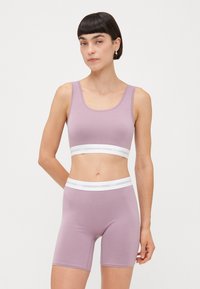 Lyse lilla sports-bh og cykeltights sæt lavet af strækbart materiale, med hvide mærke-elastiske bånd i taljen og under brystet.