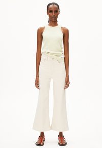 Lichtgroen geribbeld tanktop gecombineerd met off-white wijde jeans. De outfit heeft een casual ontwerp met een soepele textuur en minimale details.