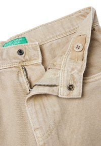 Béžové manšestrové kalhoty s rozepínáním na zip, zapínáním na knoflík a zelenou visačkou na pase. Texturovaná tkanina s viditelným žebrováním.