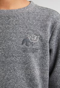 Grauer Hoodie mit rundem Halsausschnitt, aus strukturiertem Stoff gefertigt. Verfügt über ein gedrucktes Logo mit roten Akzenten auf der linken Brust.