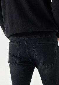 Jeans de mezclilla negra con un ajuste slim, que cuentan con dos bolsillos traseros y detalles de costura sutiles. El material parece suave pero duradero.