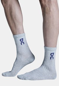 Chaussettes grises en crew fabriquées à partir d'un matériau texturé, arborant un logo violet. Le design comprend des bords côtelés et une finition lisse.