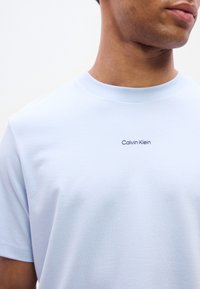 Ανοιχτό μπλε βαμβακερό μπλουζάκι με στρογγυλή λαιμόκοψη. Διαθέτει μικρό λογότυπο «Calvin Klein» σε σκούρο μπλε, τοποθετημένο στο κέντρο του στήθους. Απαλή υφή.