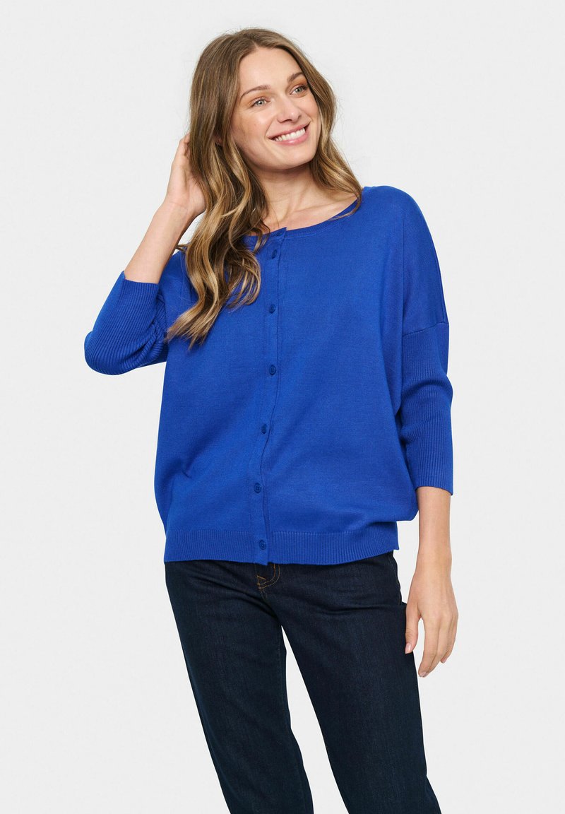 Blue cardigan with a round neckline, seven buttons down the front, and three-quarter length sleeves. Soft knit material with ribbed cuffs.