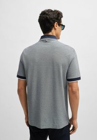 Grå pikétröja med marinblå detaljer, korta ärmar och en texturerad tyg. Har en klassisk krage och en liten logga på baksidan.