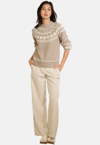 Beiger Strickpullover mit gemustertem Einsatz in Creme, kombiniert mit cremefarbenen weit geschnittenen Hosen und hellen Sneakers. Glatte Textur.