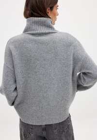 Gray turtleneck sweater with a ribbed collar and hem, made of soft material. Loose-fitting silhouette with dropped shoulders.