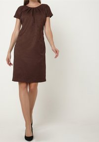 Femme portant une robe marron longueur genou avec un motif paisley subtil et des manches courtes, associée à des chaussures noires à talons hauts.
