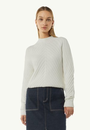 Textured white sweater with a high neck and diagonal rib pattern. Long sleeves and a relaxed fit. Paired with a dark denim skirt.