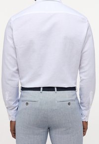 Weißes Langarmhemd mit glatter Textur und klassischem Kragen. Hellblaue, maßgeschneiderte Hose mit Taschen und dezenten Details.