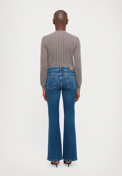 Maglione grigio a coste, aderente in vita. Jeans in denim blu a gamba larga, con vita alta e tasche posteriori, caratterizzati da dettagli di cucitura discreti.