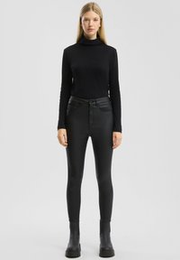 Un haut noir à col roulé à manches longues associé à un pantalon skinny en simili cuir noir taille haute et des bottes à plateforme noires, le tout sur un fond neutre.