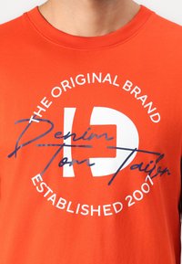 Orange bomulds T-shirt med rund hals, prydet med hvid og navy blåt grafisk tekst: "THE ORIGINAL BRAND" og "Denim Tom Tailor ETABLERT 2007."