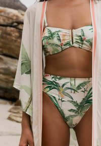Bikini-setti, jossa on trooppisia lehvipainatuksia vihreissä ja vaaleanpunaisissa sävyissä. Kevyt, teksturoitu kimono, jossa on hienovaraisia persikanvärisiä yksityiskohtia ja vapaat hihat.