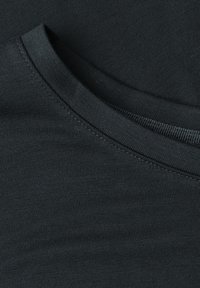 Gros plan sur un tissu noir montrant des coutures détaillées et une texture autour d'un col ou bord plié d'un vêtement.