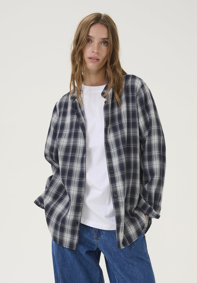 Marinero en wit geruit flanellen overhemd met een losse pasvorm, knoopsluiting aan de voorkant en lange mouwen over een wit T-shirt. Licht textuur en casual ontwerp.