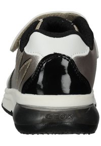 Zapatilla en blanco y negro con acentos metálicos, que presenta un talón texturizado, un cuello ceñido y una suela negra con logotipo.