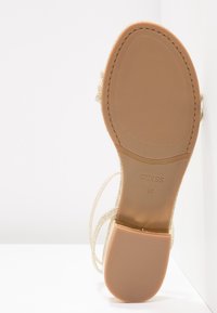 Semelle d’une sandale beige Guess avec talon bloc, affichant la taille 37 et une surface de talon antidérapante texturée.