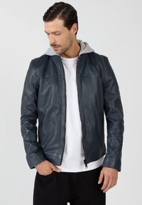 Marineblaue Lederjacke mit grauem Kapuzen, ausgestattet mit einem Rei�ßverschluss, Seitentaschen und detaillierter Stickerei auf der Brust und den Schultern.