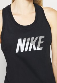 Nainen, jolla on päällään musta hihaton toppi, jossa on suuri valkoinen ja harmaa Nike-logo rinnan kohdalla.