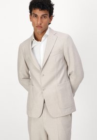 Sacou tailored bej deschis, cu două buzunare frontale și două butoane. Purtați peste o cămașă albă, are un design structurat și linii curate.