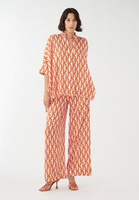 Conjunto de dos piezas que incluye una blusa suelta con cuello y pantalones de pierna ancha en un atrevido patrón geométrico de rojo, naranja y amarillo sobre un fondo claro.