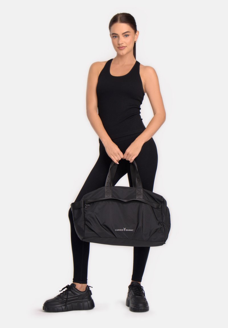 Fekete duffel táska két fogantyúval, sima anyagból készült. Elülső cipzárral és az oldalán "CARDIO BUNNY" logóval ellátva.