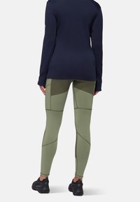 Marineblauw langemouwtop gecombineerd met lichtgroene strakke leggings met geometrische panelen en donkere schoenen.