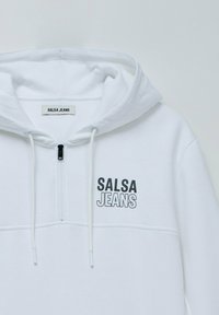 Sudadera blanca con cremallera frontal, cordón ajustable y "SALSA JEANS" impreso en negro y gris. Tejido suave, diseño informal, sin patrones.
