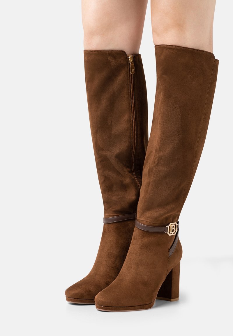 Bottes hautes en daim marron avec talons carrés, fermeture éclair latérale et bride décorative avec boucle dorée autour de la cheville.