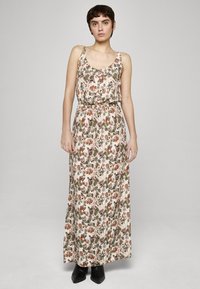 Maxikjole med blomstermønster i myke rosa, grønne og oransje nyanser. Har tynne stropper, innsvingt midje og flytende design. Svarte støvler.