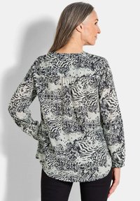 Langärmlige Bluse in einem schwarz-cremfarbenen abstrakten Muster, mit lockerer Passform und leichten Faltendetails am Rücken. Weicher, fließender Stoff.