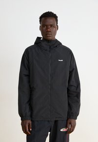 Black zip-up jacket with a hood, made of lightweight material. Features elastic cuffs and a small logo on the chest. صاف.