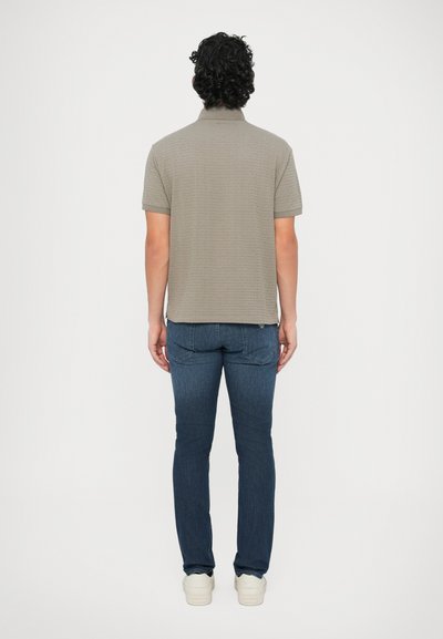 Sivá polo košeľa s krátkym rukávom a textúrovaným vzorom, doplnená tmavomodrými džínsami a bielymi teniskami, pohľad zozadu.