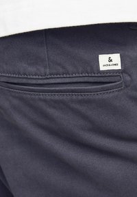 Ciemnogranatowe spodnie o gładkiej fakturze mają tylną kieszeń oraz małą białą metkę z logo "JACK & JONES."