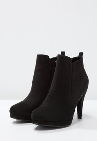 Černé kotníkové boty z měkkého semiše, s vysokým podpatkem, kulatou špičkou a bočním zipem. Hladký povrch s minimem švů.