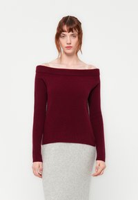 Ο μπορντό πουλόβερ με ανοιχτούς ώμους σε μαλακό πλεκτό ύφασμα με μακριά μανίκια, συνδυασμένο με μια ελαφριά γκρι εφαρμοστή πλεκτή φούστα.