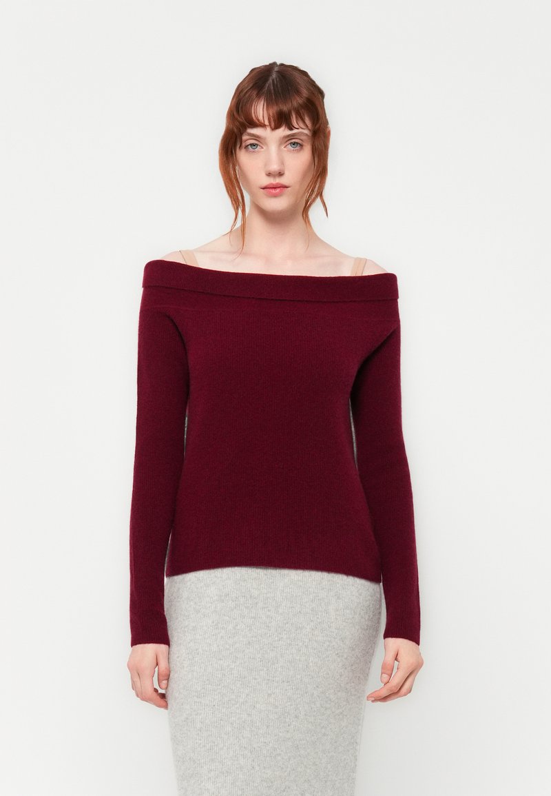 Ο μπορντό πουλόβερ με ανοιχτούς ώμους σε μαλακό πλεκτό ύφασμα με μακριά μανίκια, συνδυασμένο με μια ελαφριά γκρι εφαρμοστή πλεκτή φούστα.