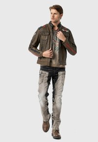 Bruine leren jack met rode accenten, twee borstzakken en gestructureerde mouwen. Draag over een grijs graphic T-shirt en versleten lichte jeans.