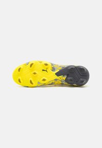 Suela de zapato deportivo Puma en amarillo y gris, con una superficie texturizada y patrones moldeados, además de elementos de tracción de goma en negro.