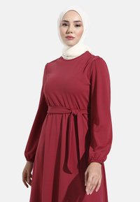 Rode lange mouwen jurk met een ronde halslijn en een ceintuur om de taille. Gemaakt van gladde stof, met gathersleefden en een vloeiende silhouet.