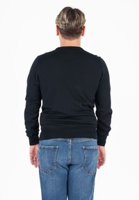 Maglione nero a maglia con scollatura rotonda, polsini e orlo a coste; indossato con jeans in denim blu dotati di tasche posteriori e dettagli di cucitura.