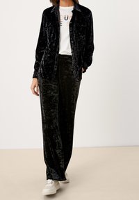 Camicia di velluto nero e pantaloni abbinati con una finitura morbida e texturizzata; abbinati a scarpe bianche con suola scanalata.