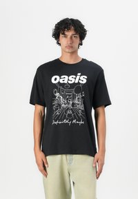 Sort bomulds T-shirt med fed hvid tekst, der står "oasis" samt et skitseret design nedenunder med teksten "Definitely Maybe." Løs pasform.