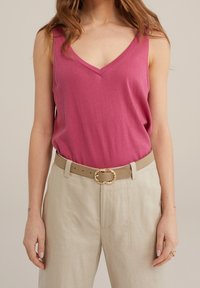 Rosa bomullstopp med V-ringning, ihop med ljusbeige linbyxor och ett tan-bälte med en gyllene, vriden spänne.